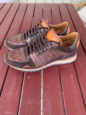 Magnanni Brown Crocodile Sneakers  - Exklusiva Magnanni sneakers i brun krokodilpräglad design med subtila orange detaljer. Elegant silhuett med tydlig luxury runner-känsla inspirerad av klassiska designer sneakers. Väldigt hög kvalitet och premiumkänsla rakt igenom. Nypris cirka 450$.      Strl 44