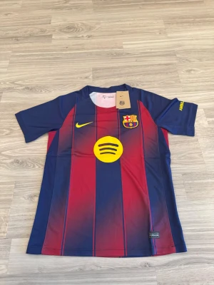 Barcelona hemmaställ 25/26  - Säljer en officiell FC Barcelona matchtröja från Nike med klassiska röda och blå vertikala ränder. Tröjan har klubbmärke på bröstet, gul Nike-logga och Spotify som sponsor framtill. Tillverkad i lätt och ventilerande material, perfekt för fotboll eller träning.