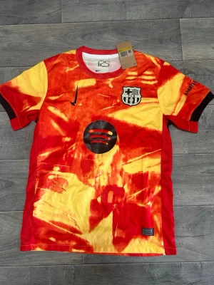 Barcelona (ICE peach Tea) - Säljer en Barcelona matchtröja från Nike i röd och gul tie-dye design. Tröjan har klubbmärke, Nike-logga och sponsortryck på bröstet samt tryck på ärmarna. Tillverkad i lätt och ventilerande material, perfekt för fotbollsträning eller match.