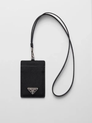 Svart kortfodral med rem från Prada - Stilrent svart kortfodral från Prada med en lång rem att hänga runt halsen. Fodralet har en klassisk rektangulär form och är tillverkat i ett strukturerat lädermaterial. Prada-loggan i silver sitter på framsidan och ger en lyxig känsla.