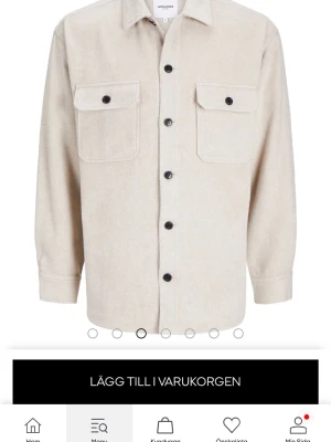 Beige overshirt från Jack & Jones - Stilren beige overshirt från Jack & Jones med raka linjer, två stora bröstfickor med lock och svarta knappar framtill. Perfekt lager-på-lager-plagg i mjukt material och klassisk passform. Enkel att matcha med olika outfits.