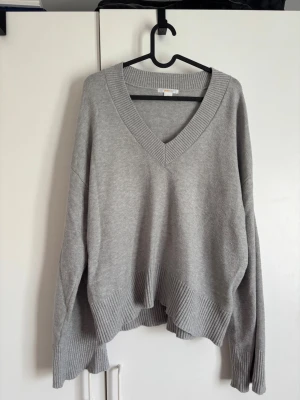Grå stickad tröja från Gina Tricot🫶🏻 - Mysig grå stickad tröja från Gina Tricot med djup V-ringning och bred ribbad kant vid hals, ärmslut och nederkant. Tröjan har en avslappnad passform och längre ärmar, perfekt för lager på lager och chill stil. Jätte skön!🤍