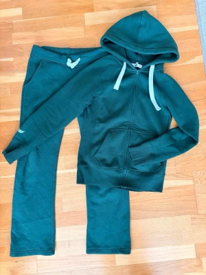 Mörkgrönt Russemerch set - Jättefint mjukissett från Russemerch. Både tröja och byxor i stl Xs. Jättekonstigt ljus på bilderna men det är grönt. (färgen på bild 7 är hur de ser ut i verkligheten) ser även något fläckigt ut på bilderna men plick försämrar kvaliteten otroligt mycket.
