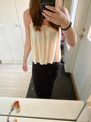 Ljusbeige  linnetopp - Säljer en ljusbeige linnetopp med tunna axelband och plisserad struktur. Toppen har en lös och flowy passform och är perfekt för varma dagar. Materialet känns lätt och luftigt, och toppen har en enkel men trendig look.
