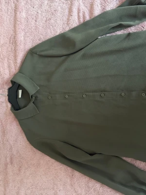 Olivgrön skjorta med knappar - Säljer en stilren olivgrön skjorta från Jaqoueline de Young med klassisk krage och knappar längs hela framsidan. Skjortan har långärmad design och är tillverkad i ett lätt och mjukt material som känns skönt mot huden. Perfekt för dig som gillar enkel och clean stil.