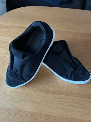 Axel arigto laceless skor  - Svarta axel arigato laceless skor med vit sula och ovandel i mocka. Skorna har elastiska band över foten för enkel påtagning och en stilren design utan snörning. Perfekt för dig som gillar en clean och sportig look. Liten defekt men inget håll in 
