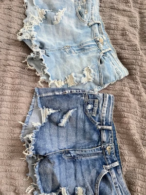 Två par slitna jeansshorts i denim - Två par snygga jeansshorts i ljus- och mörkblå denim med slitna detaljer och fransig kant. Klassisk femficksmodell med knapp och dragkedja. Perfekta för en avslappnad och trendig look. Jättestrechiga och sköna, lite för korta för min smak. Fler bilder kan ordnas om så önskas!