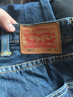 Levi's 501 blå jeans - Klassiska blå Levi's 501 jeans i rak modell med knappgylf och tydliga kontrastsömmar. Ikonisk läderpatch bak i midjan. Tillverkade i slitstark denim som ger en tidlös look.