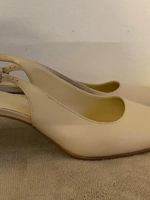Beige pumps från Daniel Hechter - Stilrena pumps i beige skinn från Daniel Hechter. Skorna har öppen häl med justerbart spänne och låg klack. Klassisk rundad tå och elegant design som passar till många olika looks.