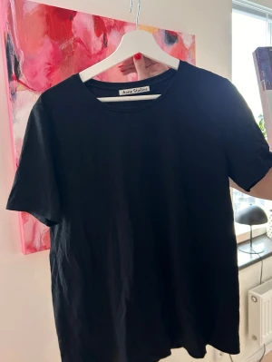 Svart t-shirt från Acne Studios - En stilren svart t-shirt från Acne Studios med klassisk rund halsringning och korta ärmar. Tillverkad i mjuk bomull som känns skön mot huden. Perfekt basplagg att matcha med allt i garderoben.