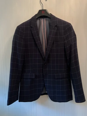 Mörkblå rutig kavaj från Zara Man - Snygg mörkblå kavaj från Zara Man med vitt rutmönster. Klassisk passform med två fickor framtill och en bröstficka. Fodrad insida med ljusa detaljer och innerficka. Perfekt för en stilren look.