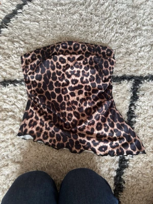Leopardmönstrad tubtopp från SHEIN - Säljer en leopardmönstrad tubtopp från SHEIN i storlek XS. Toppen är axelbandslös och har ett glansigt tyg som känns mjukt mot huden. Perfekt för dig som vill sticka ut med ett djurmönster och en trendig look.