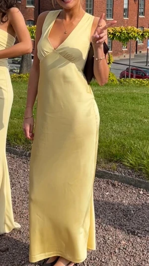Ljusgul långklänning med djup urringning och öppen rygg  - Elegant ljusgul/solgul långklänning med omlottdesign och öppen rygg. Klänningen har smala axelband och faller snyggt längs kroppen. Perfekt för bröllop eller bal. Bara använd en gång💕Nypris 1569kr