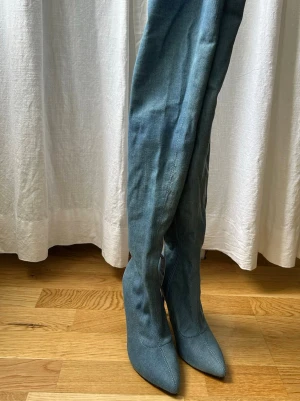 Ljusblå overknee stövletter i denim - Säljer ett par ljusblå overknee stövletter i denim med spetsig tå och smal klack. Skorna har en tight passform längs benet och en riktigt trendig siluett. Helt nya, skriv om flera bilder önskas 🥰
