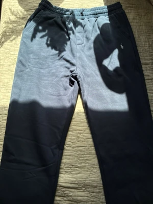 Mörkblå mjukisbyxor från Polo Ralph Lauren - Mörkblå mjukisbyxor från Polo Ralph Lauren med klassisk broderad logga på vänster ficka. Byxorna har resår i midjan och är tillverkade i mjukt, bekvämt material. Perfekta för en avslappnad stil och har en enkel, rak passform.