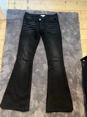 Svarta bootcut jeans med detaljer - Snygga svarta bootcut jeans med utsvängda ben och klassiska fickor. Baksidan har dekorativa sömmar på fickorna. Jeansen har normal midja och stängs med knapp och dragkedja. Perfekta för dig som gillar en trendig och bekväm stil. Jeansen är några centimeter uppsydda!!!