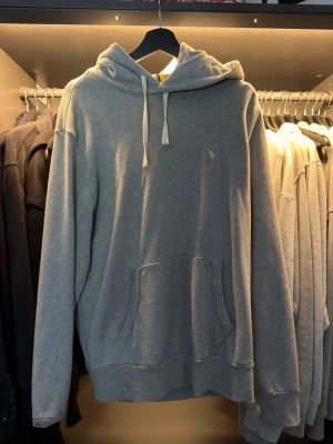 Grå hoodie från Polo Ralph Lauren - Snygg grå hoodie från Polo Ralph Lauren med klassisk huva och dragsnören. Tröjan har en broderad logga på bröstet och en stor magficka framtill. Tillverkad i mjukt bomullsmaterial och har ribbade muddar vid ärmslut och nederkant. Nypris=1600. Ändast provat då storleken var lite för stor för mig.