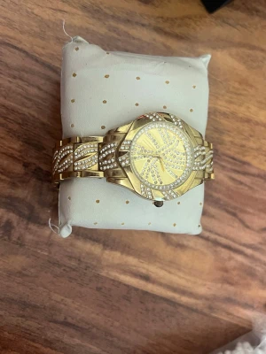 Guldig klocka med stenar och mönster - Snygg guldig klocka med glittriga stenar på både urtavla och armband. Klockan har ett unikt mönster av stenar som ger en lyxig känsla. Metallarmbandet har detaljerade mönster och passar perfekt för dig som vill sticka ut.