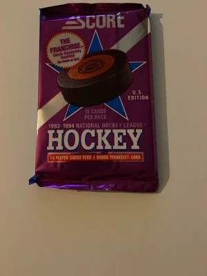 Score NHL hockeykort 1993-94 oöppnat - Oöppnat paket med 15 hockeykort från Score, säsongen 1993-1994 National Hockey League. Lila och blå förpackning med text och hockeypuck på framsidan. U.S. Edition med chans på bonuskort och specialkort.
