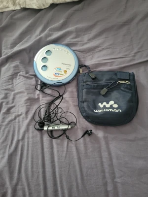 Panasonic bärbar CD-spelare med väska - Säljer en bärbar CD-spelare från Panasonic i silver och blått. Spelaren har tydliga knappar på ovansidan och kommer med hörlurar samt en blå Walkman-väska med dragkedja. Perfekt för dig som vill lyssna på CD och MP3 på språng.