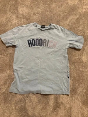 Ljusblå HOODRICH t-shirt med tryck - Snygg ljusblå t-shirt från HOODRICH i bomull med stort tryck över bröstet. Klassisk passform med korta ärmar och rund halsringning. Perfekt för en avslappnad streetwear-look.
