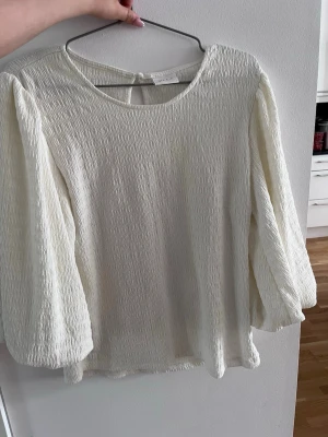 Vit plisserad blus med puffärm - Stilren vit blus från Vero Moda med plisserat tyg och rund halsringning. Blusen har långa puffärmar och en liten knappdetalj i nacken. Perfekt för dig som gillar en luftig och trendig look. Gillar super mycket men passar inte längre.😊