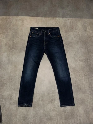 Mörkblå Levi's 502 jeans - Säljer ett par mörkblå Levi's 502 jeans med klassisk femficksdesign och raka ben. Jeansen har snygga kontrastsömmar och läderpatch bak i midjan. Tillverkade i slitstark denim med en tidlös look. Hör av vid minsta fundering