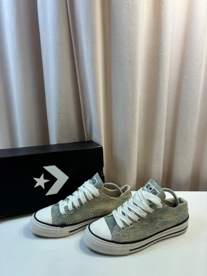 Converse Chuck Taylor sneakers - Säljer ett par Converse Chuck Taylor All Star sneakers med vit tåhätta och vita skosnören. Skorna har en slitstark canvas-ovandel med ett unikt, slitet mönster och klassisk svart rand runt sulan. Perfekta för dig som gillar en avslappnad och trendig stil.