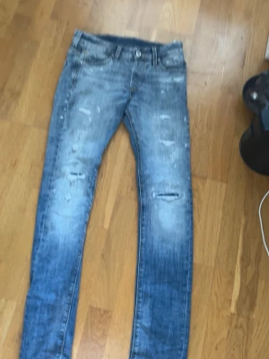 Jack and Jones Slim jeans - Säljer ett par blå slim jeans från Jack and Jones  med slitningar och distressed detaljer på både fram- och baksida. Jeansen har klassisk femficksdesign och är i stretchigt denimtyg. Perfekta för en avslappnad och trendig look.