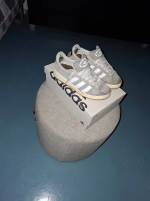 Grå Adidas campus - Snygga gråa  Adidas campus med klassiska vita ränder på sidorna. Kommer med ett par speciall sulor från stadium som är sköna och ger en mjukare känsla. Perfekta för dig som gillar en stilren och sportig look. Skorna kommer med en slitning i insida häll på båda sidor men fungerar gott som bra. Storlek 38!