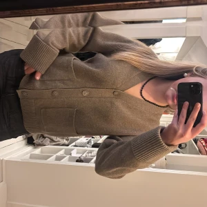 Beige kofta med knappar - Mysig beige kofta med knäppning framtill och två stora fickor. Koftan har ribbade muddar vid ärmslut och nederkant samt en avslappnad passform. Perfekt att slänga på sig över en t-shirt eller topp.