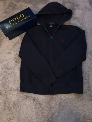 Mörkblå hoodie från Polo Ralph Lauren - Helt ny mörkblå polo Ralph lauren sip up hoodie du storlek 14-16år. Tröjan är helt ny, inga defekter eller fläckar. Nypris 1499kr. Vårt pris 499