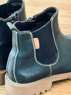 Kavat rejäla barnkängor  - Svarta kängor i läder från KAVAT med grov sula och kontrastsömmar. Resår på sidorna och dragflik bak för enkel påtagning. Märkesdetalj i brunt läder på sidan. Väl skötta och inte mycket använda, men med enstaka mindre skavmärken efter lek. 