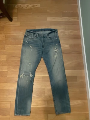 Vintage Ralph Lauren - Säljer ett par blå jeans med flera slitningar och hål på benen för en cool, avslappnad look. Jeansen är ifrån Ralph lauren denim & supply             (Är ganska osäker på längden av dem)