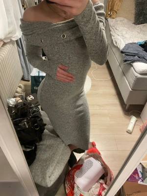 Grå offshoulder långklänning - Säljer en snygg grå långklänning med offshoulder-design och dekorativa metallringar vid halsen. Klänningen är figurnära och har långa ärmar. Den är storlek S/M. 