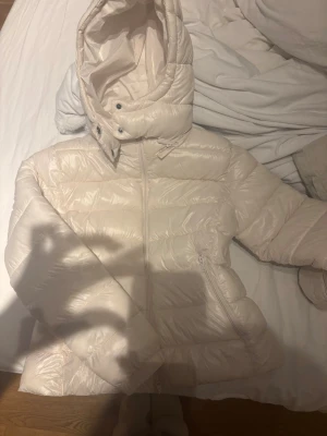 Vit dunjacka från 157 med huva - Snygg vit dunjacka från 157 med dragkedja framtill och praktisk huva. Jackan har en quiltad design och sidofickor med dragkedja. Perfekt för kalla vinterdagar och riktigt skön att bära. Materialet är glansigt och ger en modern look. Den är helt ny med pris lappen kvar. Storlek M, Nypris 400kr men säljer för 280kr. 