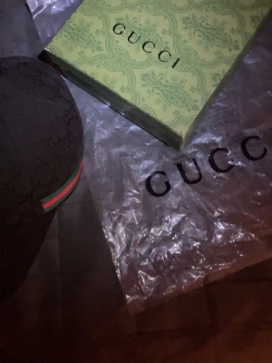 Svart keps från Gucci med monogram - Säljer en svart keps från Gucci med klassiskt GG-monogram och den ikoniska gröna och röda randen på sidan. Kepsen har böjd skärm och justerbar passform. Perfekt accessoar för en trendig streetwear-look. Priset kan diskuteras vid snabb affär. Först till kvarn!