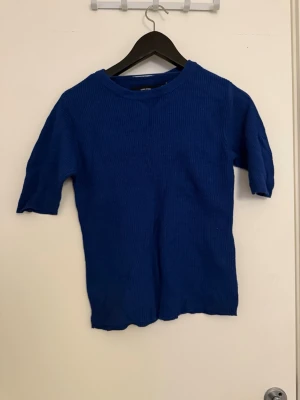 Kornblå stickad topp med kort ärm - Snygg kornblå stickad topp med rund hals och korta ärmar. Enkel och stilren design som passar perfekt till jeans eller kjol. Mjuk och bekväm stickning, perfekt för lager-på-lager-stil. M storlek men sitter som S