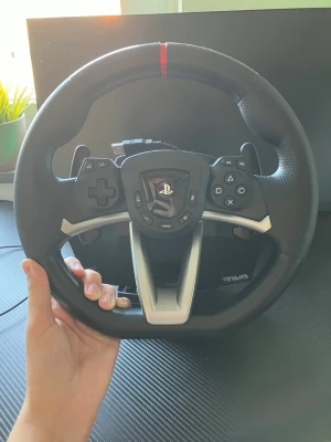 Ratt till PlayStation från Hori - Säljer en svart racingratt från Hori för PlayStation, Xbox och även PC. Ratten har PlayStation-knappar, D-pad och silverfärgade detaljer. Perfekt för bilspel och simracing, med ergonomiskt grepp och robust plastmaterial. Helt ny endast testad en gång, funkar precis som den ska men säljer den på grund av att jag ångrade köpet! Nypris ligger på ungefär 1500kr. Ratt, pedaler, sladdar och original lådan följer med!