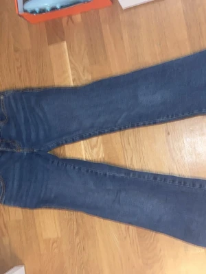 Blå bootcut jeans från Lager 157 - Säljer ett par klassiska blå jeans från 157 med utsvängda ben och dubbla knappar i midjan. Jeansen har en tidlös tvätt och är tillverkade i denim med snygga sömmar. Perfekta för dig som gillar enkel och stilren look.