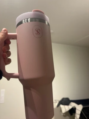 Rosa Stanley Quencher med sugrör - Säljer en rosa Stanley Quencher-mugg med handtag och sugrör. Muggen är tillverkad i rostfritt stål och plast, har en bred botten och ett lock med öppning för sugrör. Perfekt för att hålla drycken kall eller varm under dagen. Snygg och praktisk design.