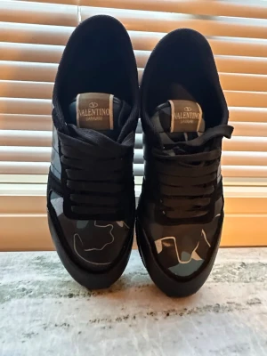 Valentino Garavani camo sneakers - Snygga sneakers från Valentino Garavani med svart och blått camomönster. Skorna har svarta snören, detaljer i mocka och läder samt en cool blå hälflik. Perfekt för dig som vill sticka ut med exklusiva och trendiga sneakers.