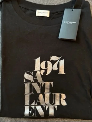 Svart Saint Laurent t-shirt 1971 - Snygg svart t-shirt från Saint Laurent med trycket '1971 SAINT LAURENT' Helt ny med alla tags. Nypris på denna är upp till 8000kr vilket gör min deal på 1749 en steal! Perfekt till sommarn och våren. Hör av dig vid fler frågor eller funderingar!