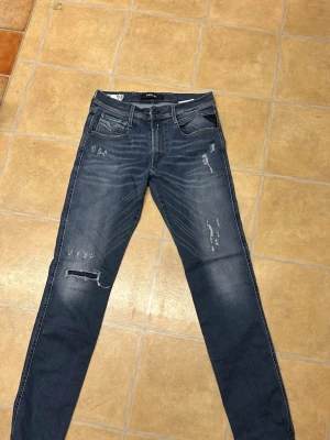 Blå slitna jeans med skinny fit - Säljer ett par blå jeans med skinny fit och slitna detaljer på både fram- och baksida. Jeansen har klassisk femficksmodell, låg midja och snygga slitningar för en trendig look. Perfekta för dig som gillar en avslappnad och modern stil.