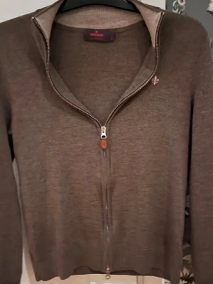 Brun stickad ziptröja från Morris - Snygg brun stickad tröja från Morris med hel dragkedja framtill och diskret logga broderad på bröstet. Tröjan har lång ärm, ribbade muddar och en klassisk rak passform. Perfekt till lager på lager och enkel att matcha.