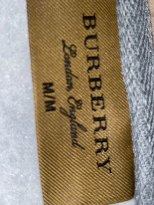 Grå zip up burberry storlek M män - Snygg grå hoodie från Burberry med dragkedja framtill och klassisk huva. Hoodien har ribbade muddar, fickor på magen och diskret Burberry-logga broderad på bröstet. Tillverkad i mjukt material som känns riktigt skönt mot huden. Perfekt för en avslappnad och trendig look.
