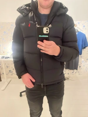 Svart dunjacka från Polo Ralph Lauren  - Säljer en svart dunjacka från Polo Ralph Lauren i ny skick . Jackan har huva och dragkedja framtill. Jackan har även två sidofickor med dragkedja och en bröstficka med den ikoniska  logga bredvid . Puffig modell som håller dig varm under kalla dagar med en grish looke  Nypris 5700 kr mitt pris 4700 kr. Hör av er för mer bilder. 