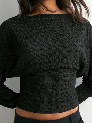 Svart topp - Trendig svart croppad topp med lång ärm och snyggt strukturerat tyg. Toppen har en tight passform i midjan och lösare upptill, vilket ger en cool siluett. 