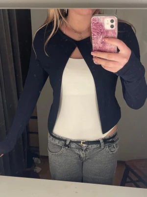 Mörkblå cropped kofta - Säljer en mörkblå, långärmad cropped kofta med öppen front och enkel knäppning vid halsen. Koftan har en smal passform och är perfekt att slänga över ett linne eller t-shirt. Materialet känns mjukt och stretchigt.