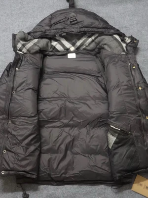 Svart dunjacka från Burberry - Snygg svart dunjacka från Burberry med klassiskt rutigt foder i huvan. Jackan har dragkedja och knappar framtill, två sidofickor med dragkedja och en avtagbar huva. Perfekt för kalla vinterdagar och riktigt stilren look.